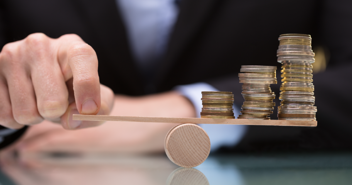 A wooden scale with two stacks of coins on one side and a finger fold down the other side
