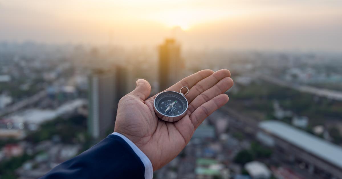 Hand holding compass with a city landscape behind