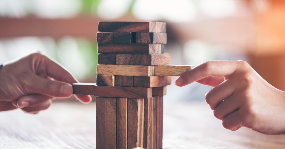 Two hands pulling blocks from Jenga tower