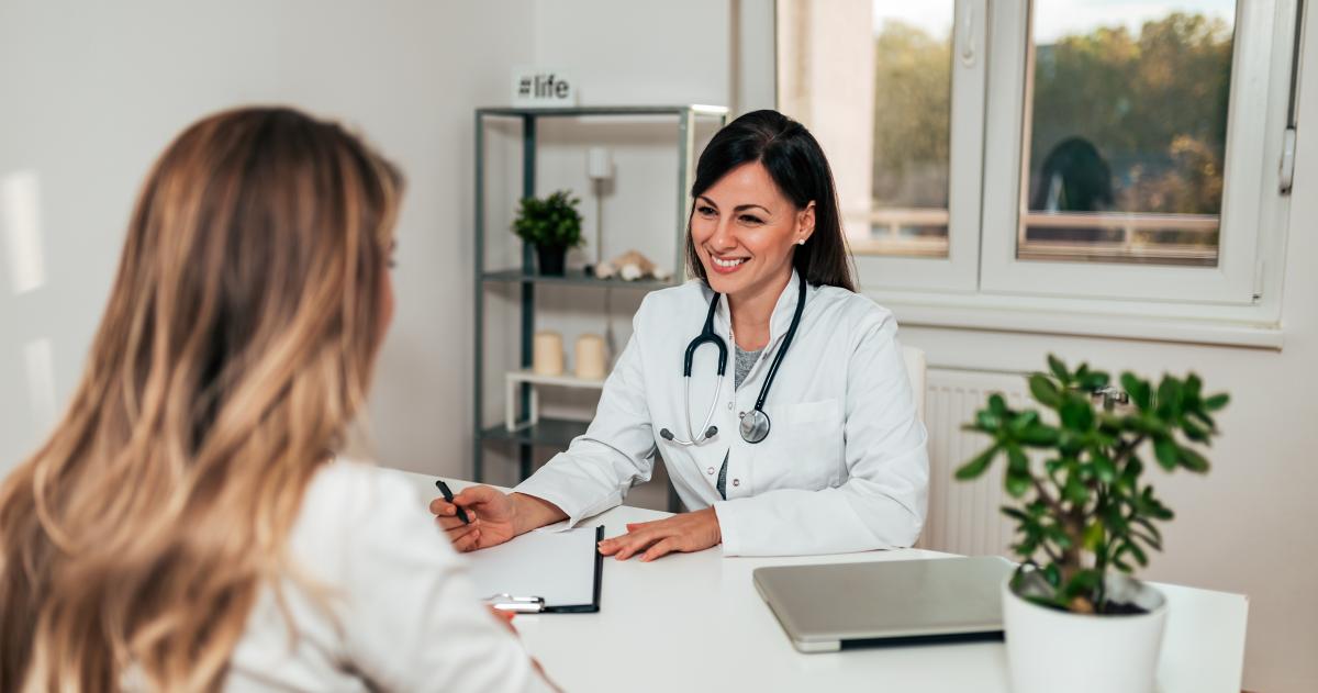 Female doctor behind a desk speaking to a female patient