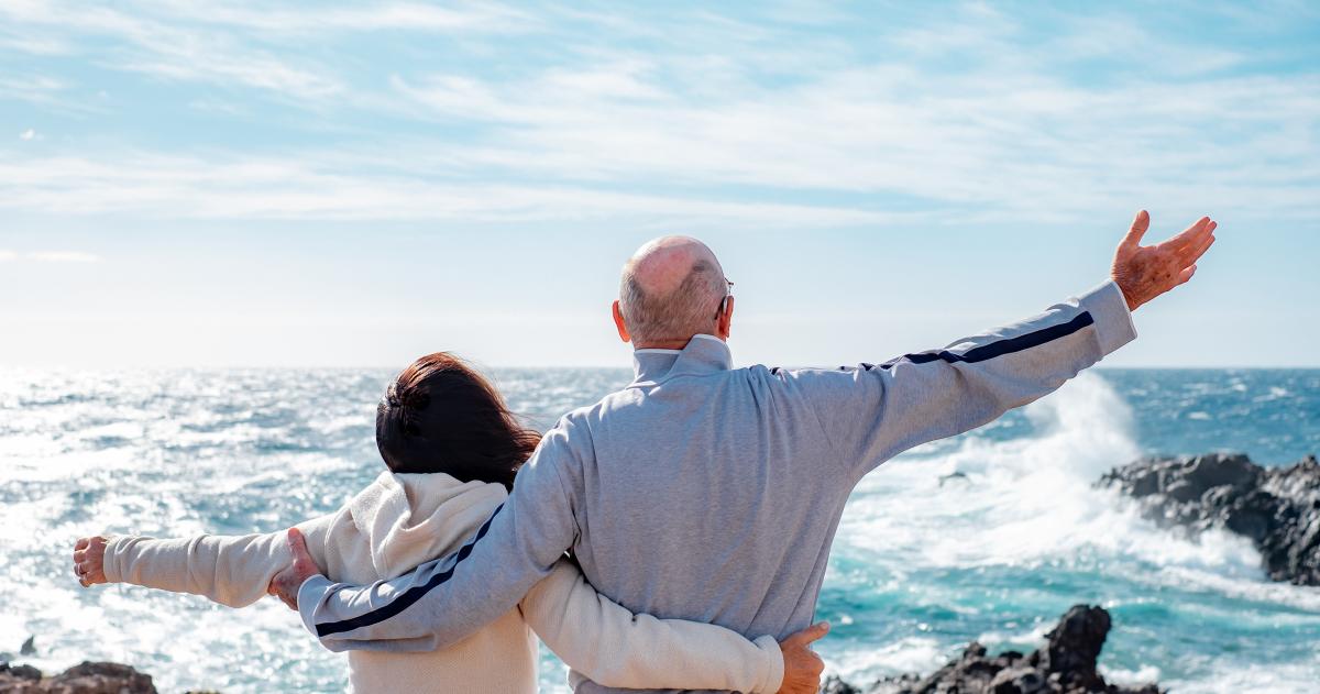 Rear view of older man and woman with arms around each other out in nature