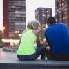 Two people in athletic clothing sit with the city buildings in front of them