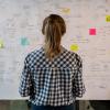 Woman with ponytail standing in front of white board with lots of notes and post-its 