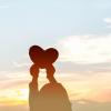 Outline of child holding up a heart shape against the sky
