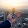 Hand holding compass with a city landscape behind