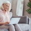 Older woman with pink blouse sitting on couch looking at laptop