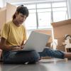 Woman sitting on floor amid moving boxes with a laptop