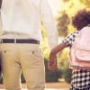 Dad and daughter viewed from behind holding hands, with briefcase and backpack