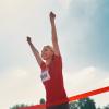 Woman in red running shirt crossing finish line with her arms in the air